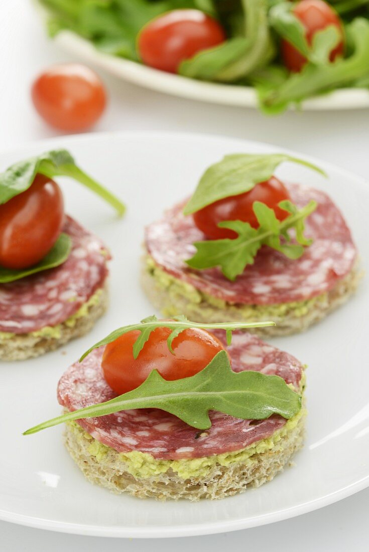 A plate of canapes with tapenade, salami, cherry tomatoes and rocket