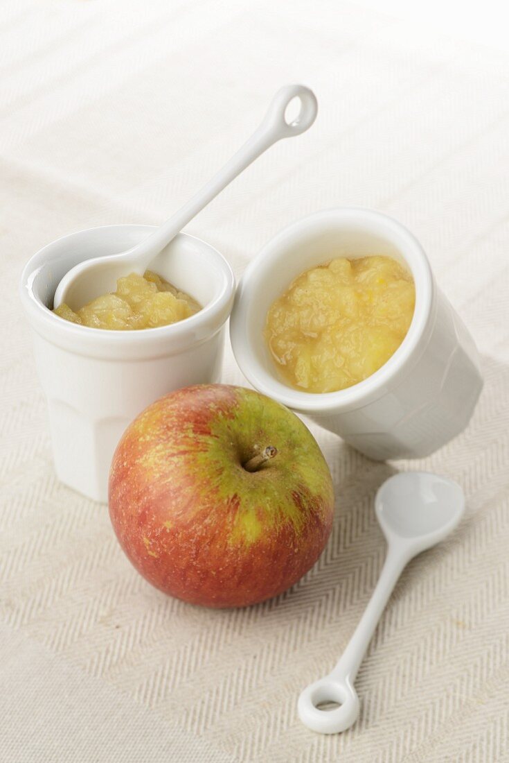 Two small bowls of apple sauce and an apple