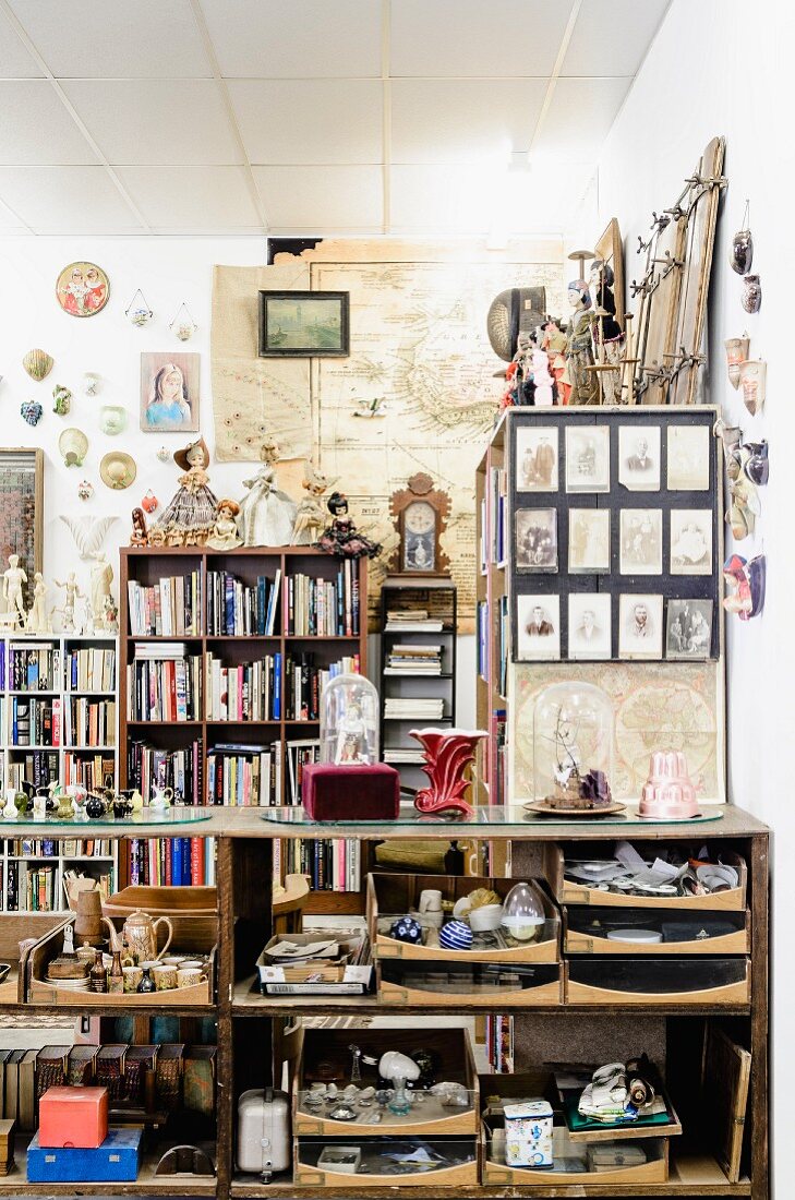 Half-height shelves full of objets d'art and bookcases against wall in cluttered room