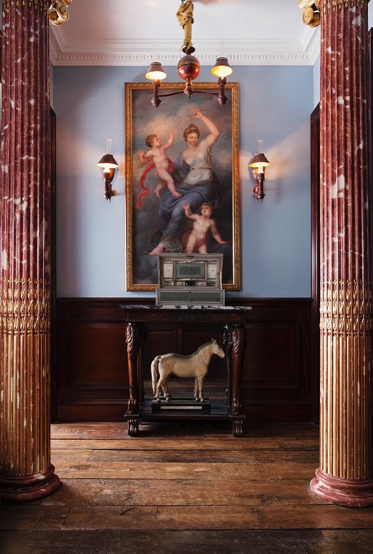 Blick zwischen zwei Marmorsäulen auf Konsolentisch mit Pferdefigur unter Gemälde im Stil der alten Meister