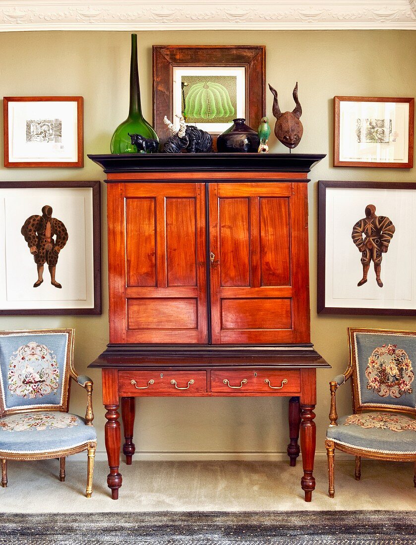 Antique mahogany bureau flanked by Baroque armchairs and framed pictures on wall