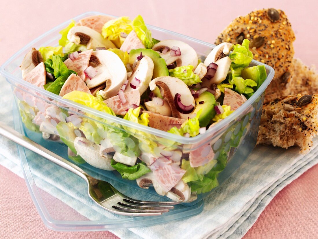 Mixed leaf salad with sausages, mushrooms and avocados in a plastic container