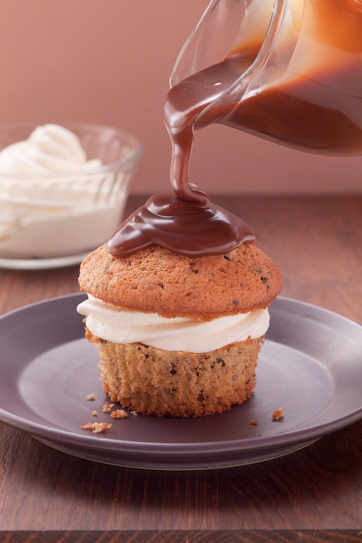 Muffin mit Creme gefüllt, mit Schokoladenglasur übergießen; Creme im Hintergrund