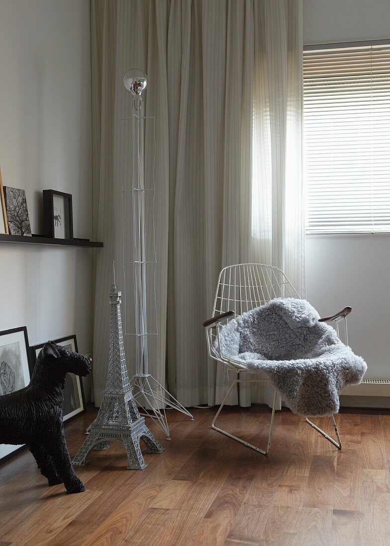 Collection of artworks in corner of bedroom: black plastic dog figure, model of Eiffel tower, wire chair and wire lamp