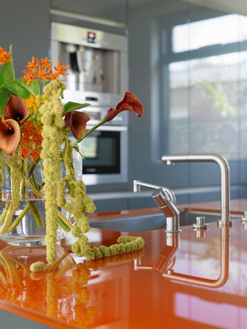 Designerküche mit orangefarbener Arbeitsplatte und Blumenstrauß mit Callas in Glasvase