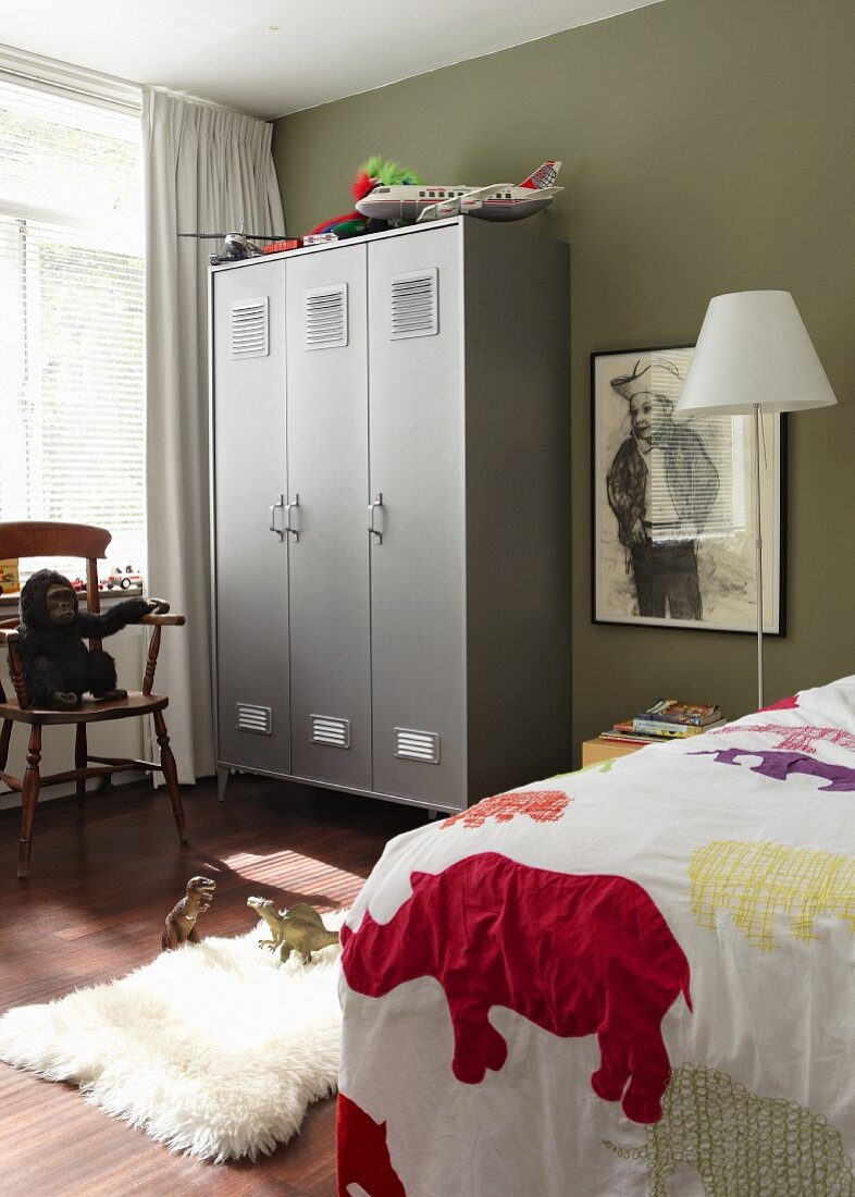 Boy's bedroom with grey locker, framed picture of young cowboy on olive green wall and animal patterned bedspread on bed