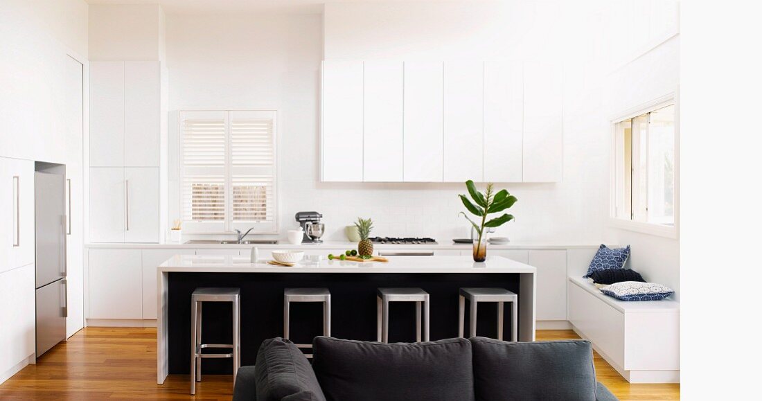 White fitted kitchen in architect-designed house with bar stools under kitchen counter on natural wooden parquet flooring