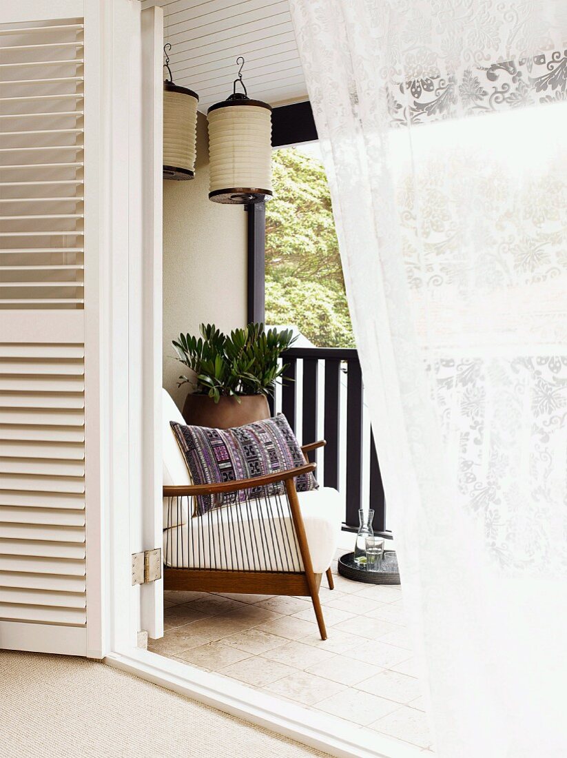 View into comfortable loggia with 50s armchair and lanterns hanging from ceiling in summery ambiance