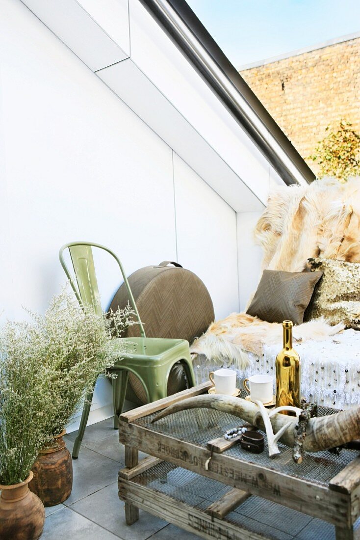 Bretterkiste mit Hasendraht als rustikaler Couchtisch und Wildlife-Accessoires wie Moschusochsenhorn und Tierfell für den Sitzplatz auf einer Dachterrasse