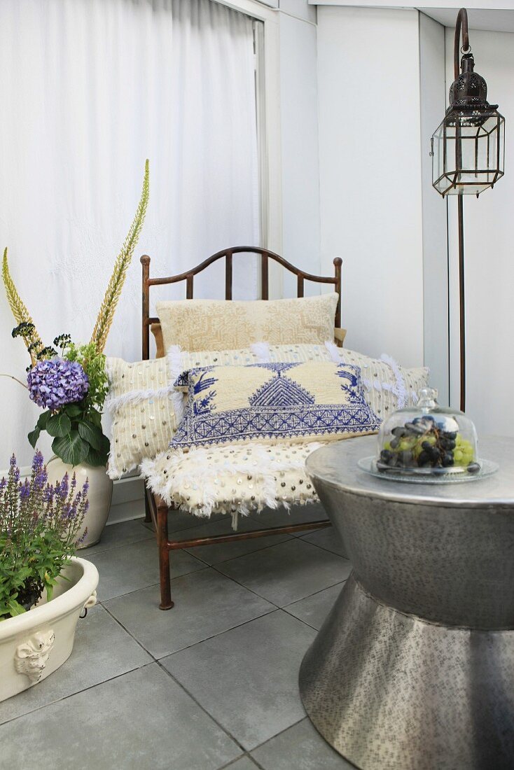 Hammered metal coffee table, wire armchair with embroidered cushions and lantern-shaped lamp as Oriental furnishings on roof terrace