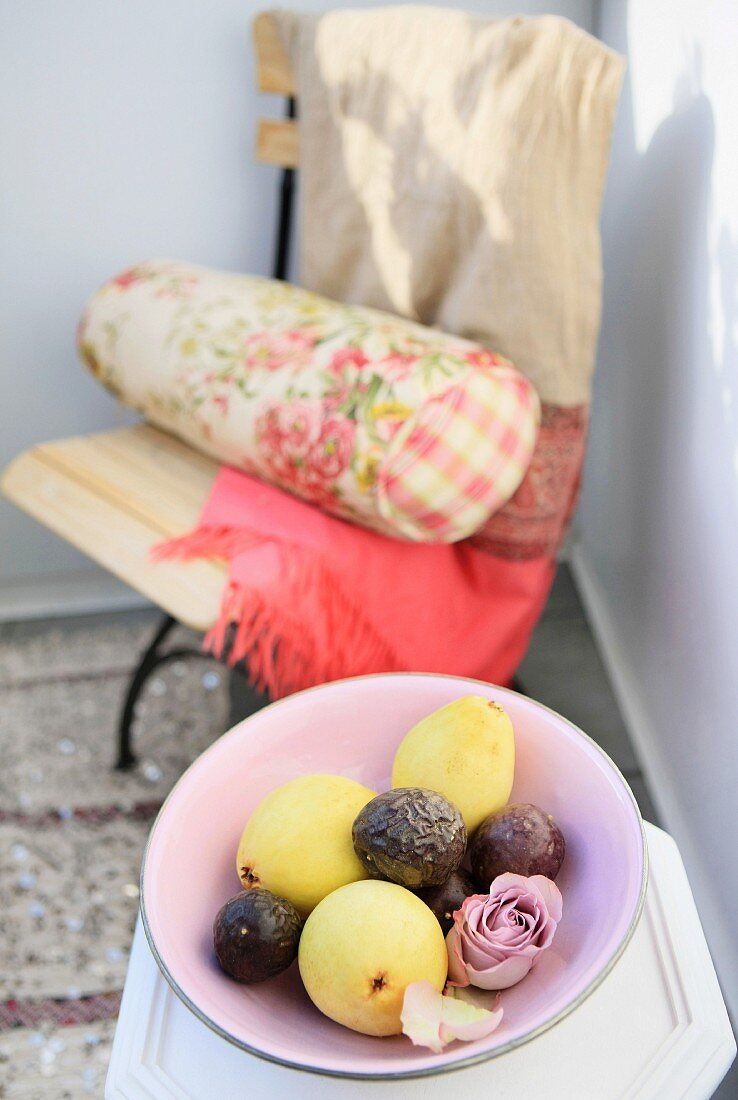 Fruit and rose in dish; garden chair with Oriental blanket and floral bolster in blurry background