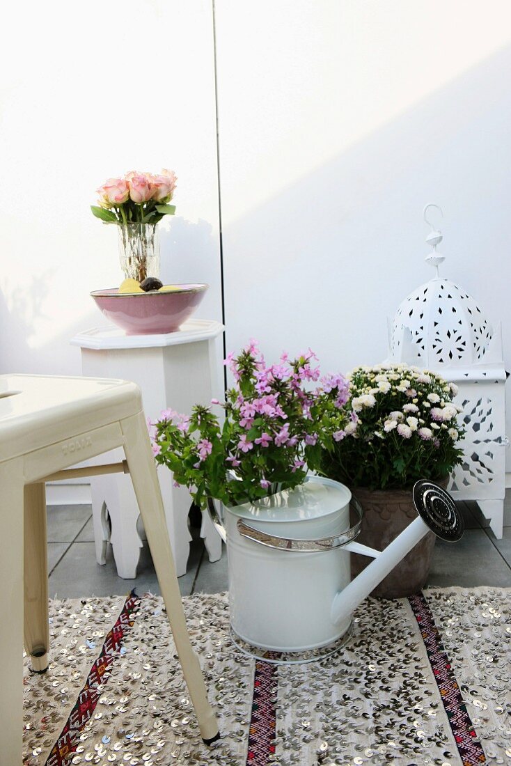 Bouquet of phlox in watering can on sequinned rug, white Marrakesh lamp and side table in background create Oriental atmosphere on roof terrace