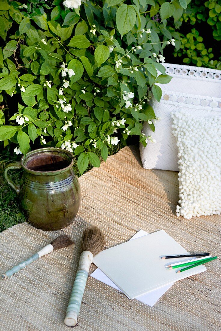 Painting utensils and paper next to jug on rug in garden
