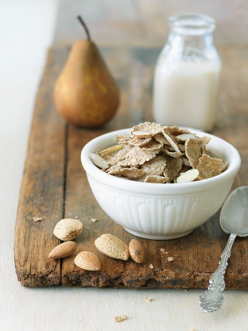 Bran Cereal with Almonds in a White Bowl; Bottle of Almond Milk; On a Cutting Board