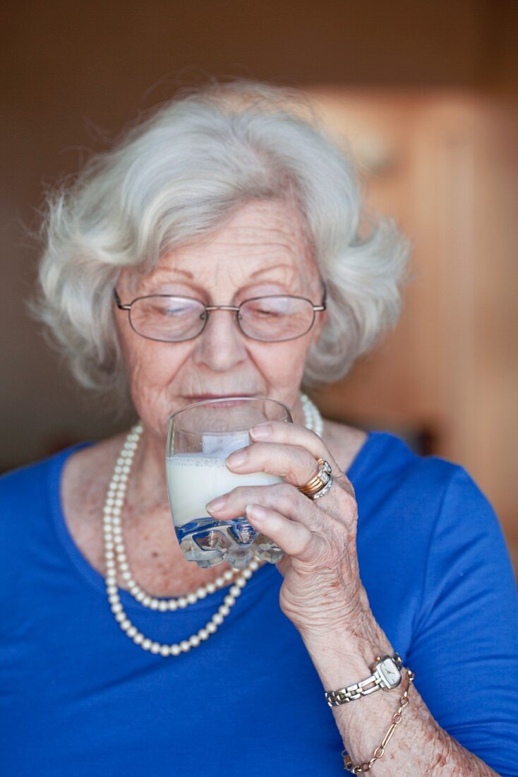 An older woman drinking a glass of milk