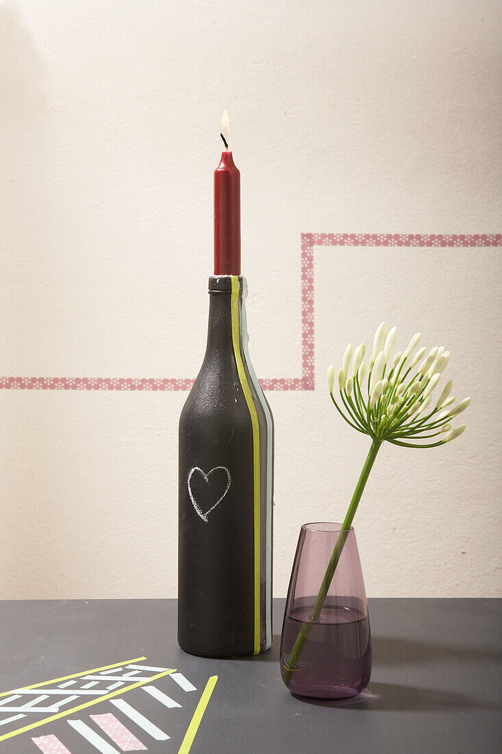 DIY candle holder made from a wine bottle next to a vase with a single flower