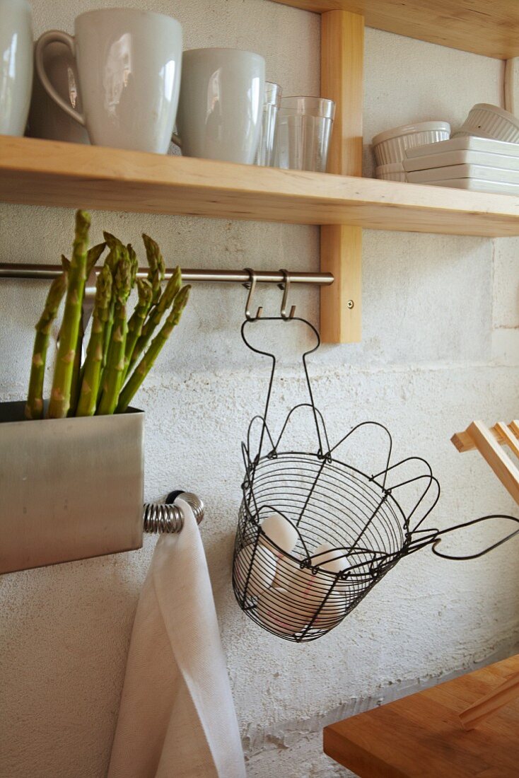 Green asparagus in sink and wire basket of fresh eggs below crockery on shelf