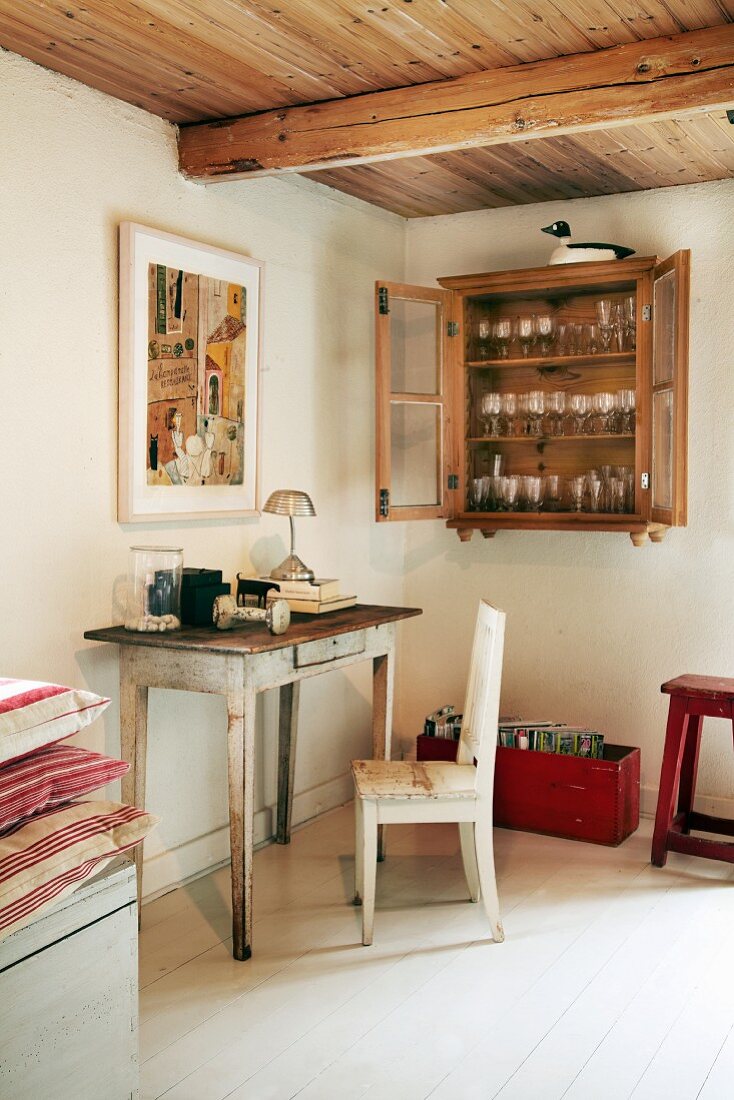 Small secretary table with chair and glasses in wall-mounted cabinet