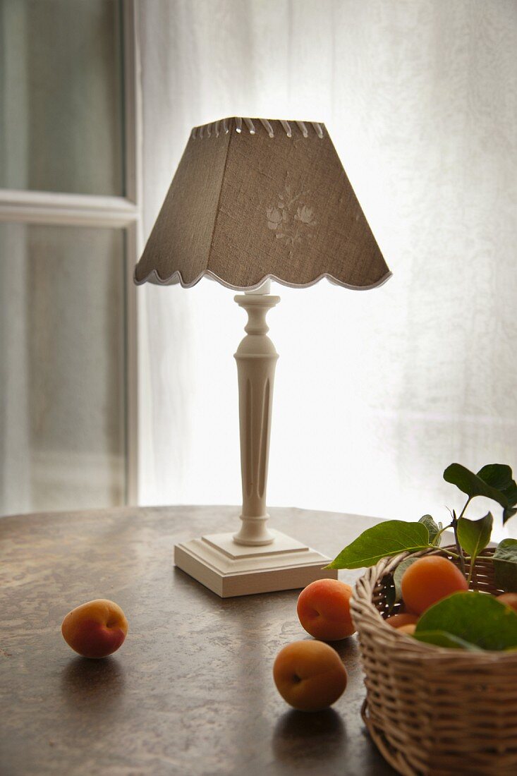 Apricots on table and in wicker basket in front of county-house-style table lamp