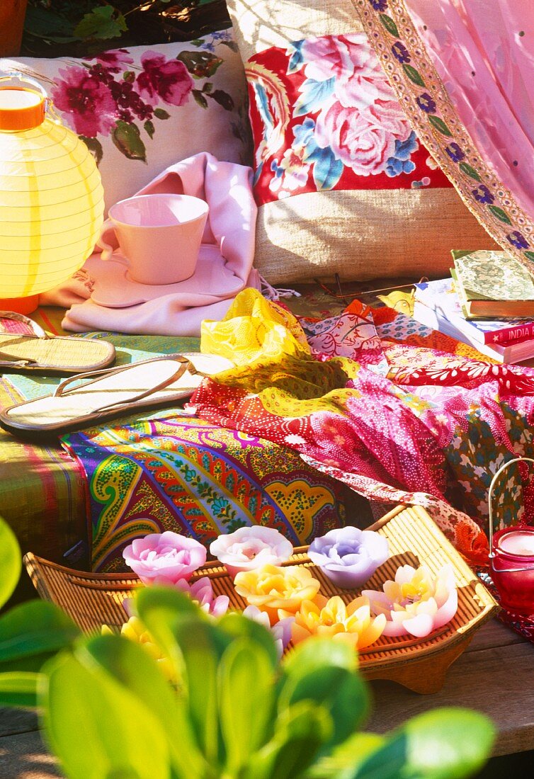 Blumenförmige Schwimmkerzen, Sitzbank mit bunten Decken, Flip-Flops, Kaffeetasse und Kissen im Freien