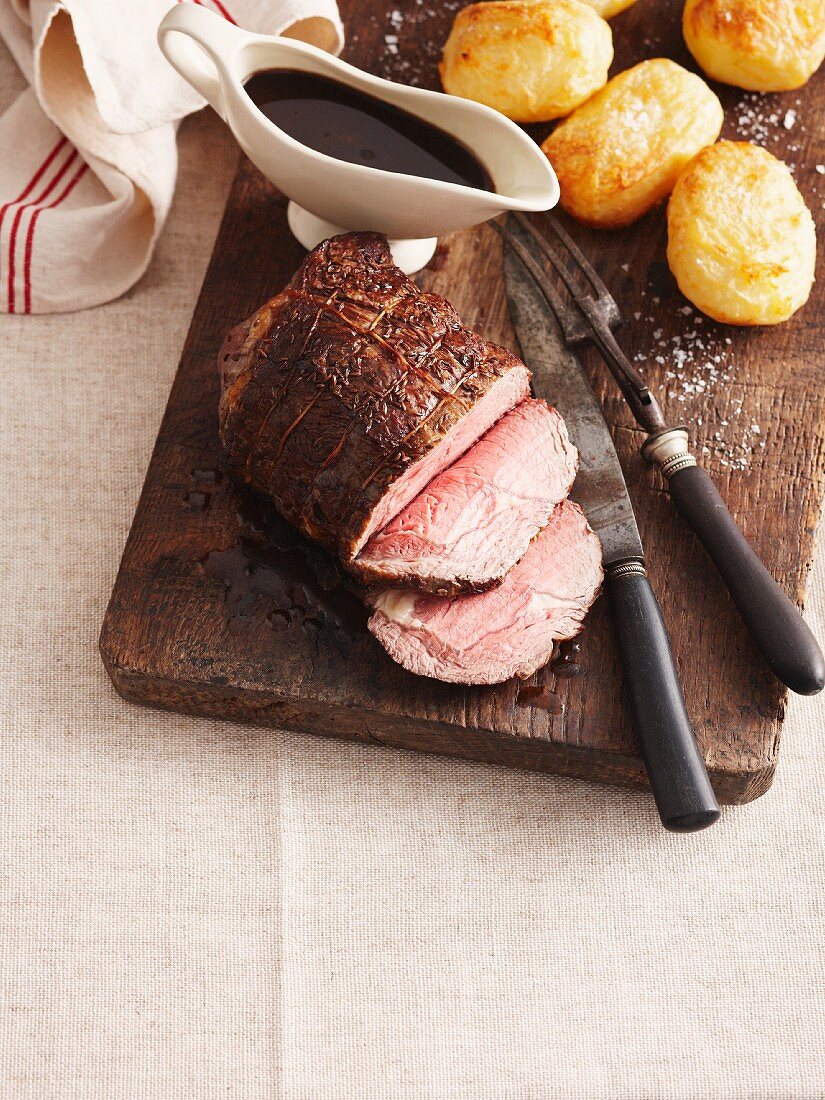 Roast beef with a Port wine sauce and roast potatoes on a wooden board