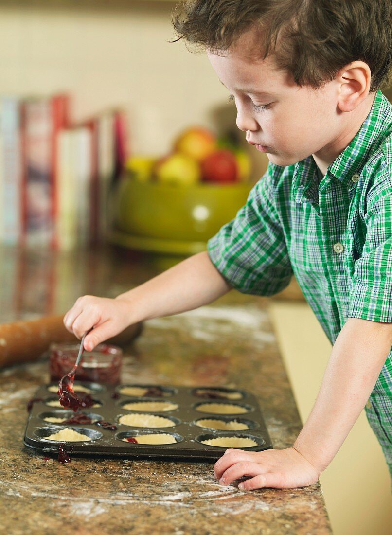 Kleiner Junge füllt Marmelade in die Vertiefungen eines Muffinblechs