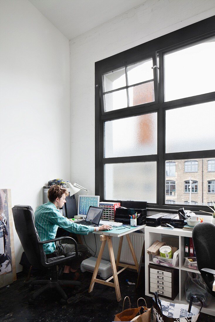 Young man sitting at laptop in front of bedroom window