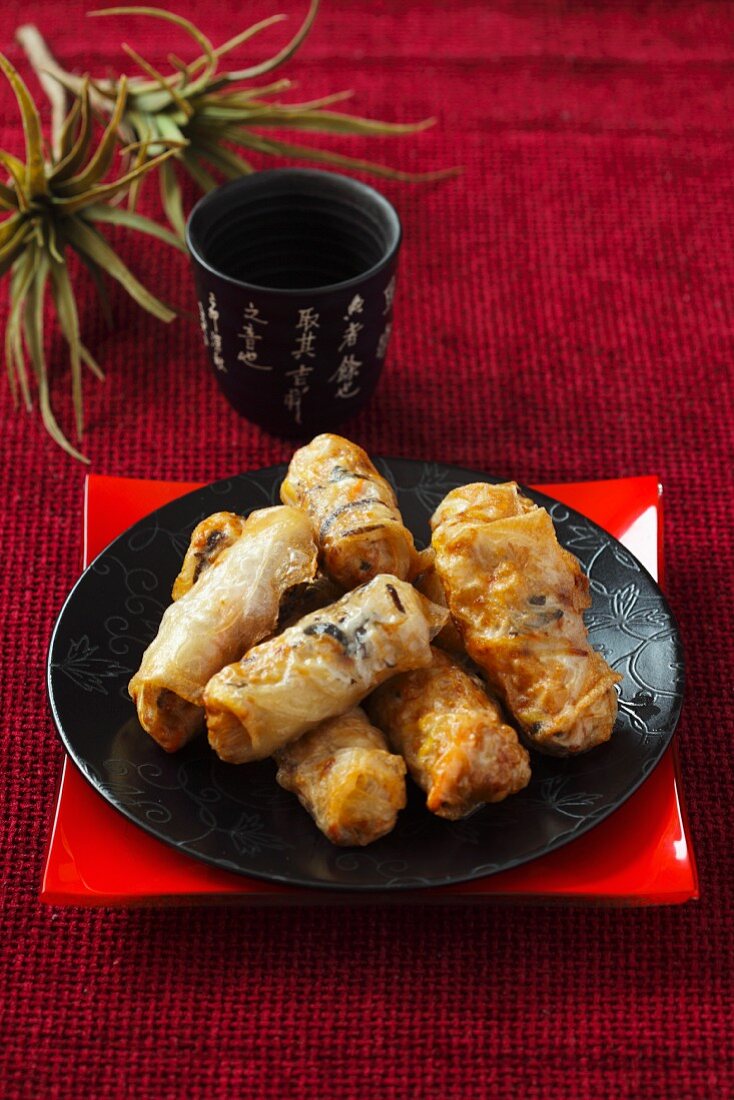 Fried spring rolls on a black plate on a red surface