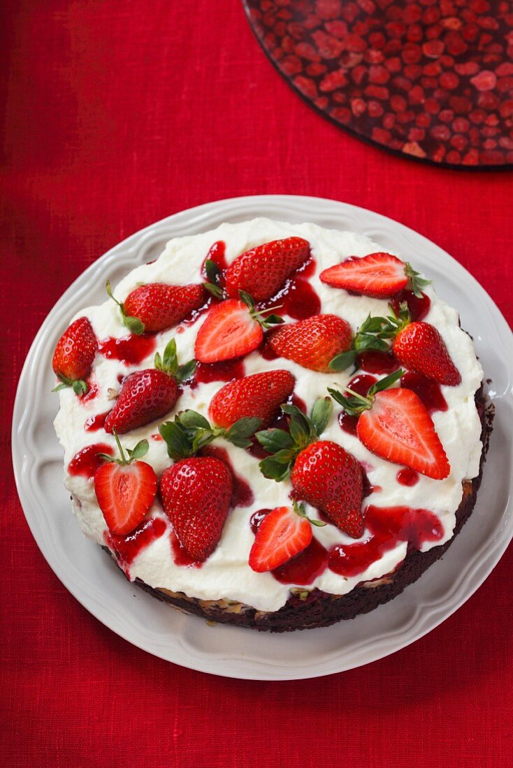 A cream cake with dark base topped with strawberries on a table with a red cloth