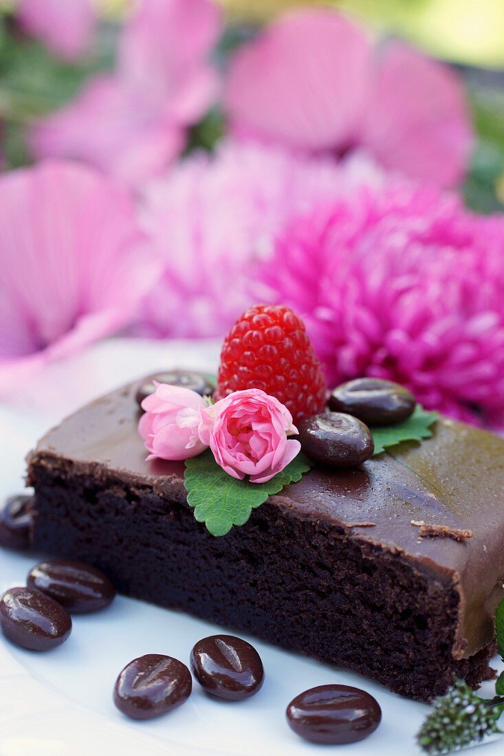 A slice of chocolate cake decorated with chocolate coffee beans and flowers