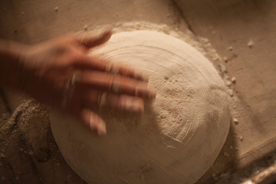 Hand bestreut ungebackenes Brot mit Mehl