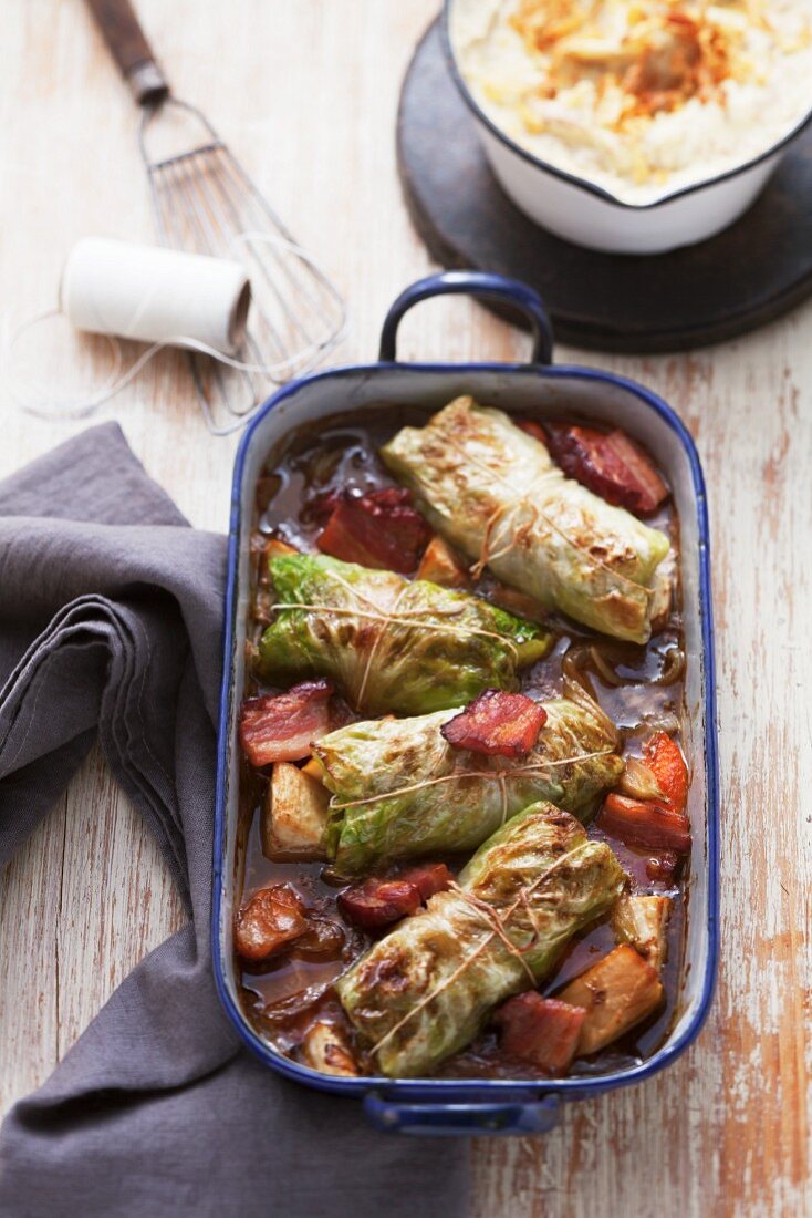 Cabbage roulade in a roasting dish with vegetables, seen from above