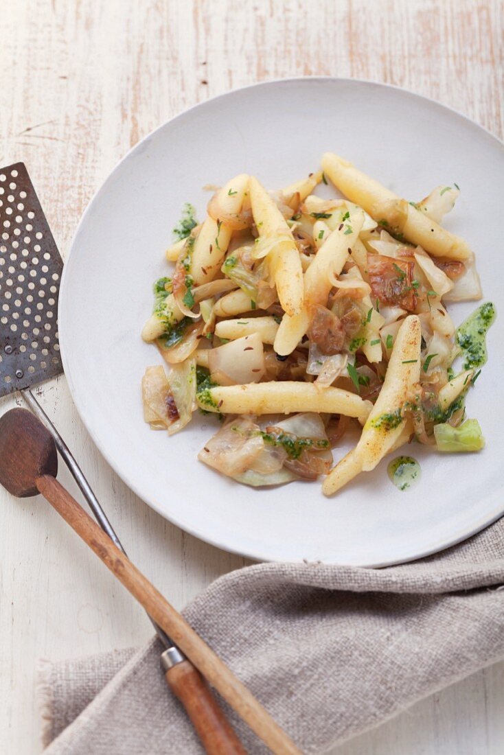 Fried potato orzo pasta with cabbage and herbs on a white plate, seen from above