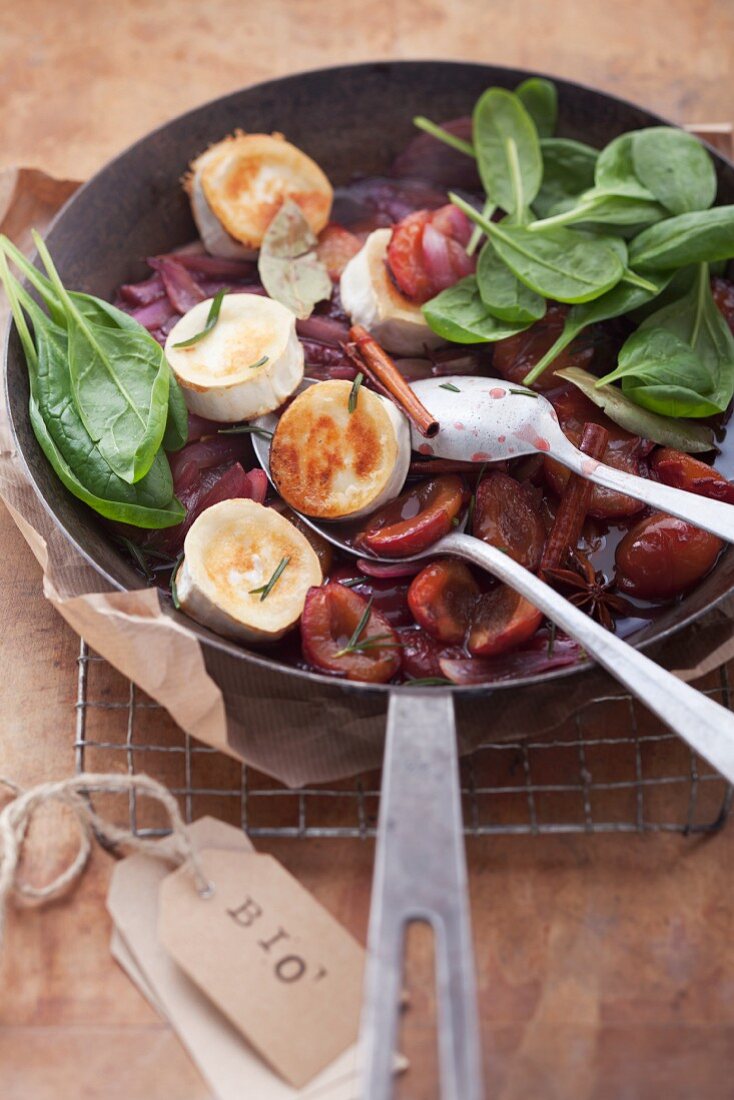 Plum compote with roasted goat's cheese and fresh spinach in a pan