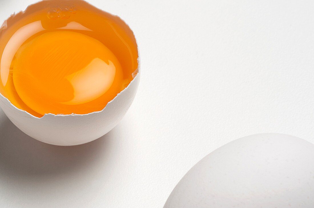 Two eggs on a white surface, one whole and one broken open