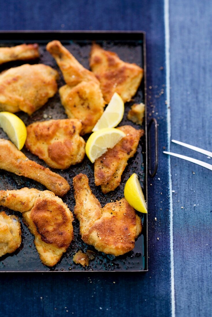 Baked chicken pieces with lemon wedges on a baking tray