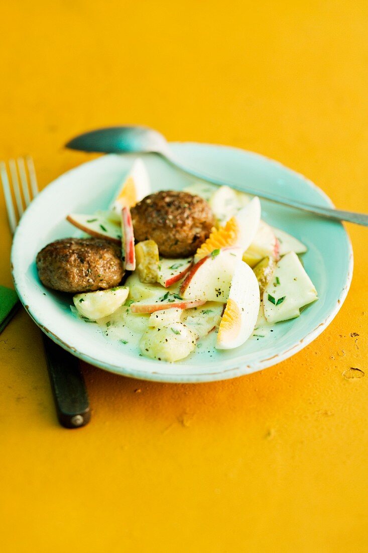 Potato salad with apple and egg, served with meatballs