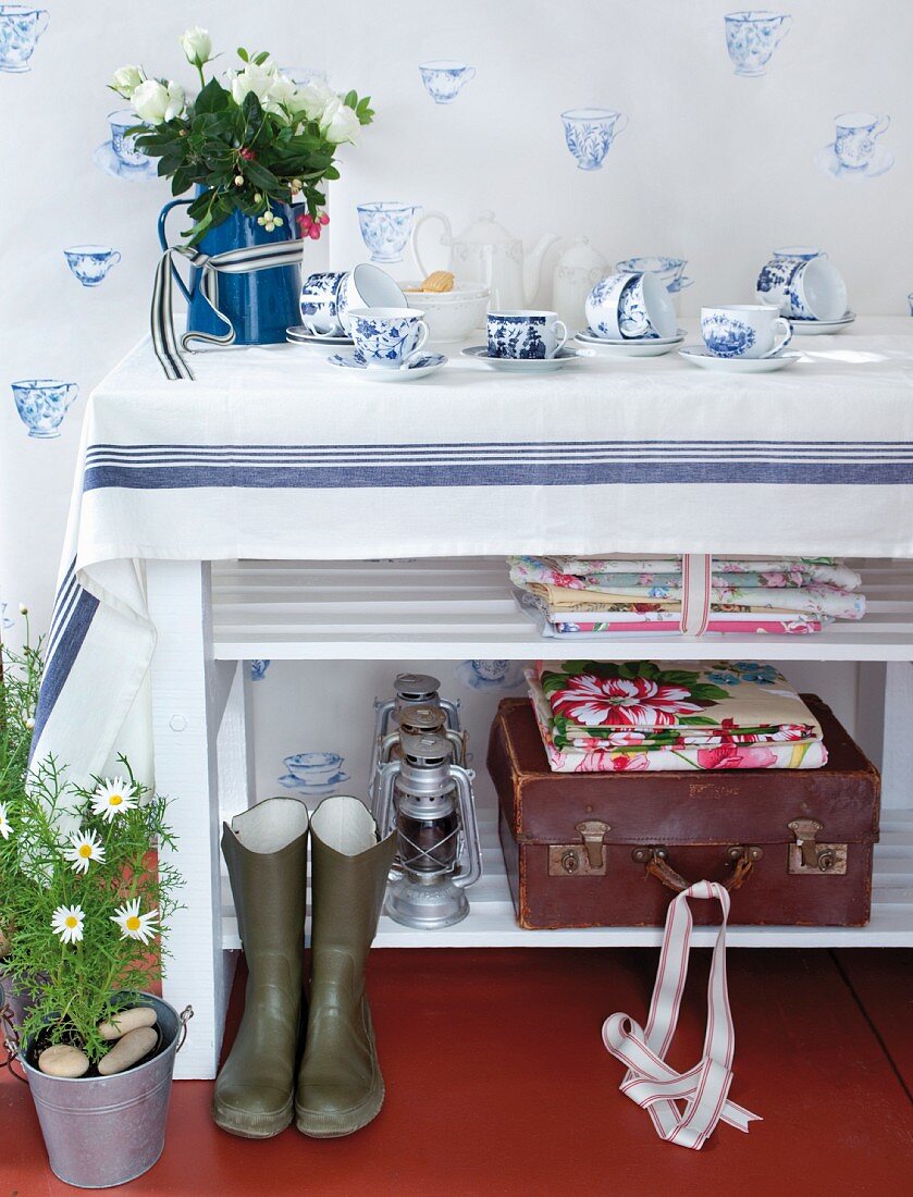 Classic white and blue crockery on shelf and as wallpaper motif; floral fabrics and vintage suitcase