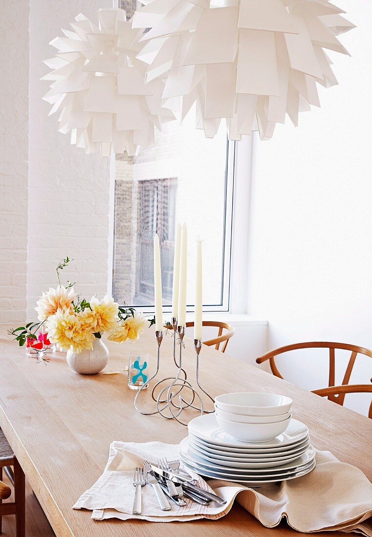 Crockery and table decorations on natural-finish wooden table below two designer pendant lamps