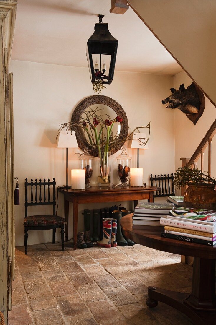 Brick floor in traditional hallway of English hunting lodge with lantern-style lamp, hunting trophy on wall and foot of staircase