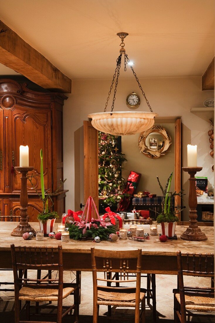 Festively decorated dining table and rustic, rush bottom chairs below traditional bowl lampshade hanging from chains
