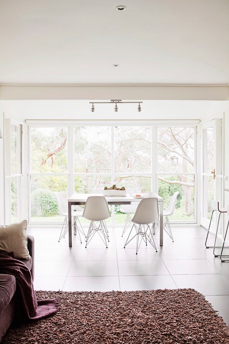 Dining table with white Eames chairs in front of a large glass front