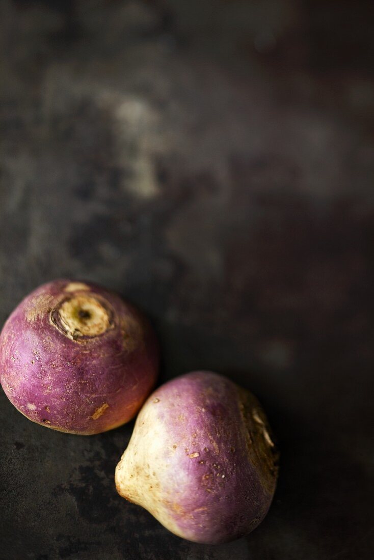 Two turnips on a dark surface