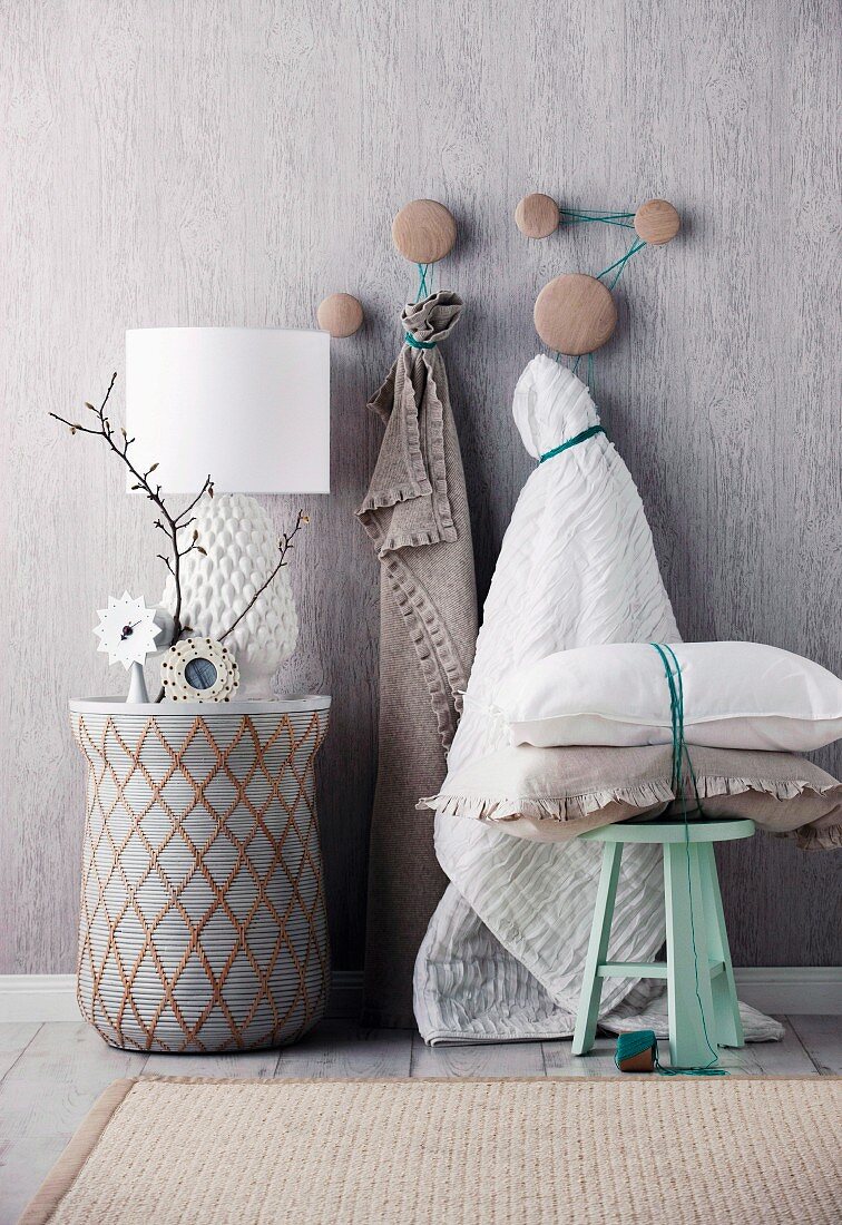 Gray wall with a table in front in the form of a drum; Pillows stacked on a pastel green stool