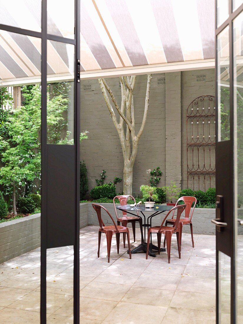 View of retro-style, coloured, metal chairs at round table in courtyard through open terrace door