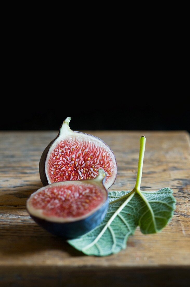 A halved figs with a fig leaf on a wooden surface