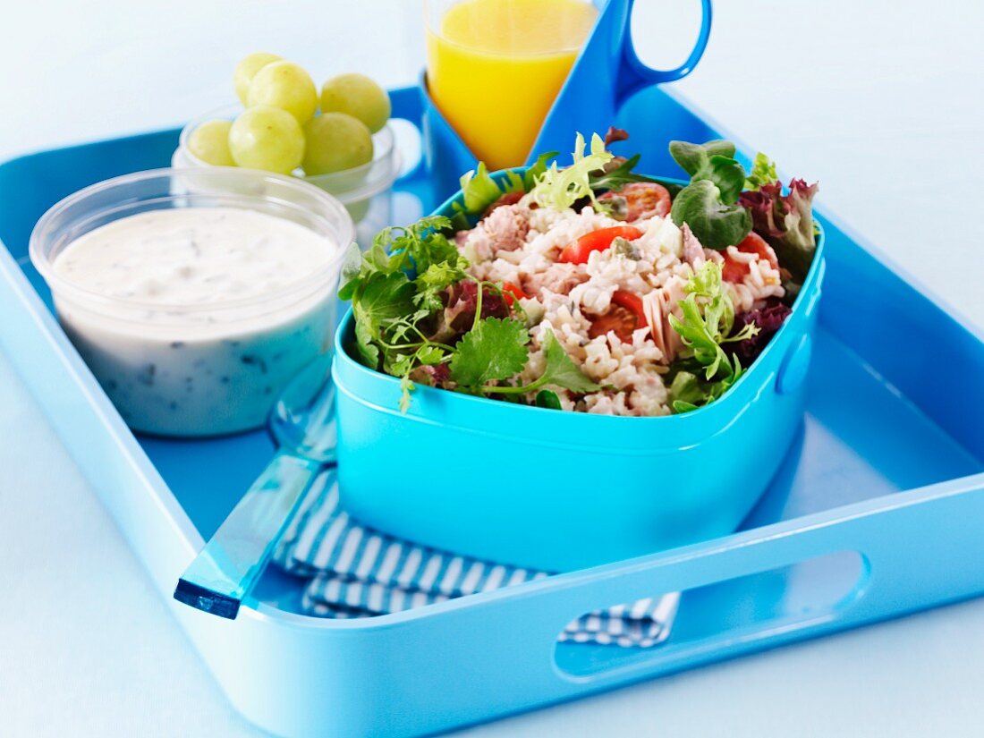 Rice salad, sauce, grapes and orange juice in a lunchbox