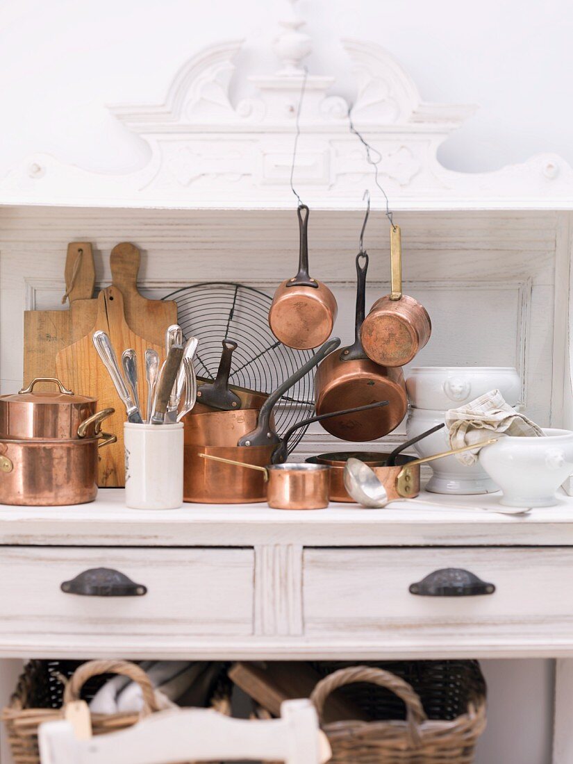 Various copper pots and kitchen utensils on a white wooden dresser