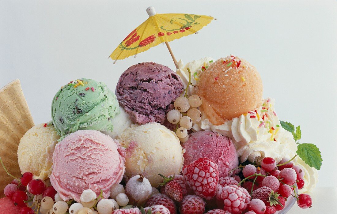 Various scoops of ice cream, frozen berries, cream and a cocktail umbrella