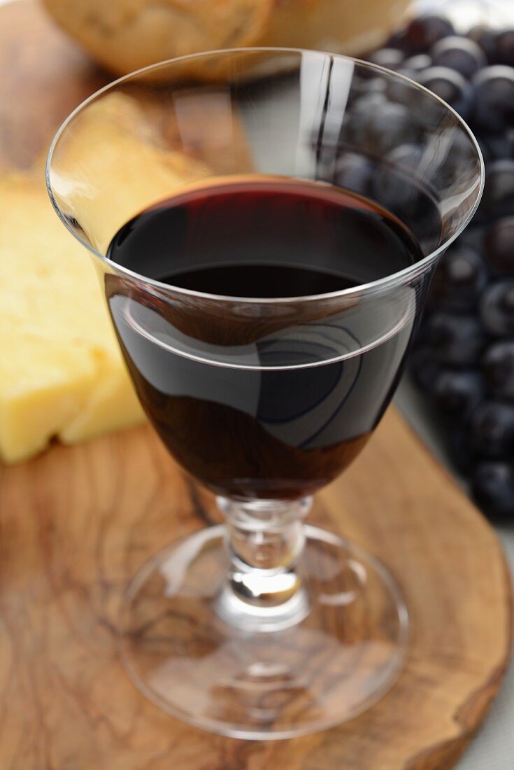 Rotweinglas, im Hintergrund Käse, Trauben und Brot